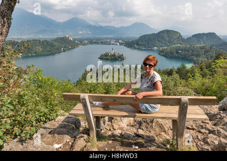 Âge moyen blanc femme bronzée s'asseoir sur banc en bois avec vue de dessus du lac. Osojnica de montagne en Slovénie. Banque D'Images