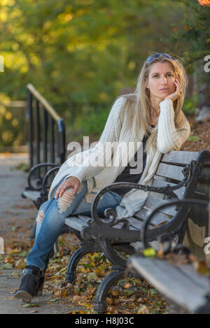 Attractive blonde jeune femme assis sur un banc dans le parc à l'arrière-plan flou Banque D'Images