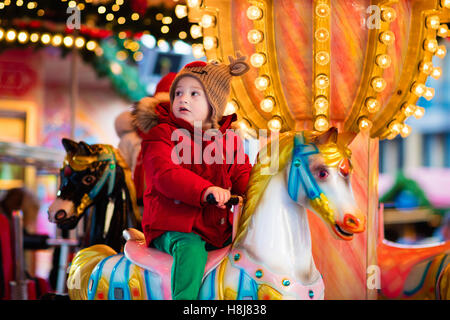 Heureux petit garçon en veste chaude et rouge nordique tricoté bonnet et écharpe riding carousel horse au cours de voyage en famille Banque D'Images