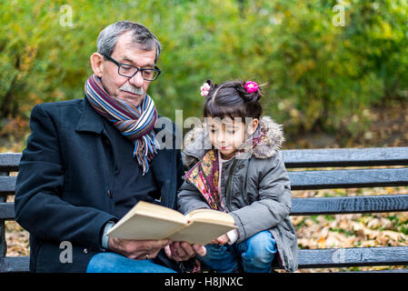 Grand-père et petite-fille de lire un livre à l'automne park Banque D'Images