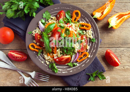 Produits bio frais et tomates Salade de couscous aux légumes et les verts - salade végétarienne saine sur table en bois rustique Banque D'Images