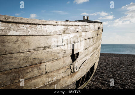 Coque d'un vieux bateau de pêche d'aviron en bois en décomposition avec les trous de sur une plage de galets au bord de la mer Banque D'Images