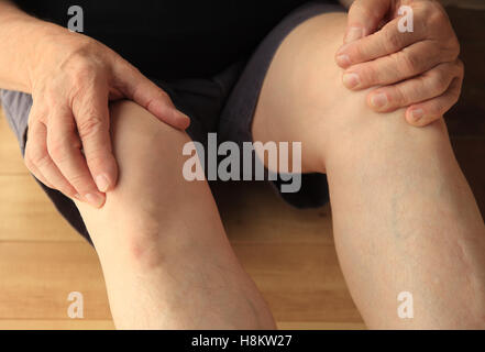 Un homme âgé est assis sur le sol avec ses mains sur ses genoux. Banque D'Images