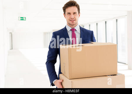 Portrait of young businessman carrying cardboard boxes in new office Banque D'Images