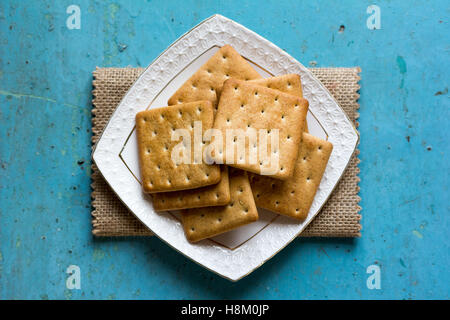 Biscuits Craquelins dans une soucoupe carrée en céramique blanche sur lin serviette sur fond bleu vieux de près. Vue d'en haut Banque D'Images