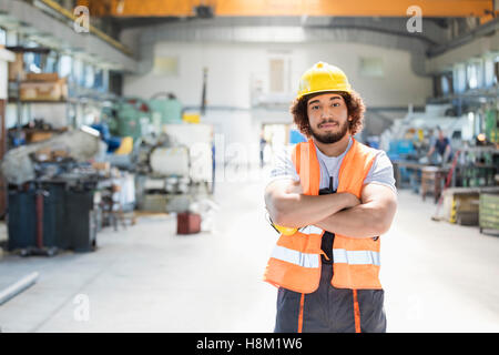 Portrait de jeune travailleur manuel standing arms crossed in factory Banque D'Images