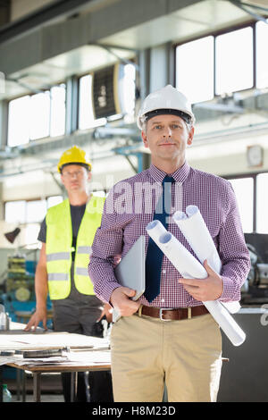 Portrait of male architect holding blueprints et ordinateur portable avec en arrière-plan à l'industrie