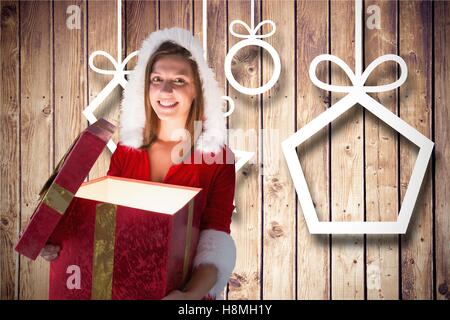 Smiling woman in santa costume d'ouvrir sa boîte-cadeau contre fond de bois Banque D'Images