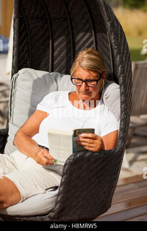 Senior woman reading book in hooded chaise de plage Banque D'Images