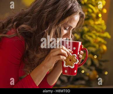 Biscuits de Noël sont une façon merveilleuse de profiter de l'esprit de la saison. Jeune femme ayant une tasse de chocolat chaud avec des guimauves et cookie dans l'arbre de Noël d'avant Banque D'Images