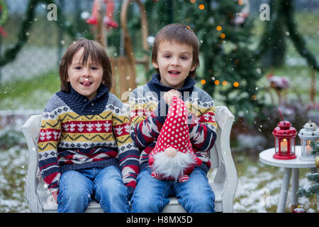 Deux adorables enfants, garçon frères, s'amusant à l'extérieur dans le jardin à Noël autour de l'arbre de Noël décoré tout en sn Banque D'Images