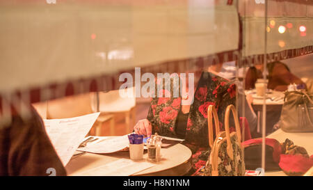 Un couple par la fenêtre d'un bistrot à l'intermédiaire de leurs menus. D'autres clients peut être vu dans le restaurant à l'arrière-plan. Banque D'Images