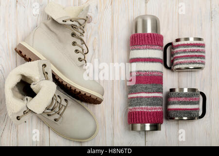 Lumière d'hiver bottes et un thermos dans la couverture en tricot sur le fond lumineux en bois. Banque D'Images