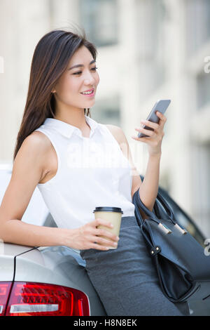 Confiant Chinese businesswoman leaning on car avec smart phone Banque D'Images