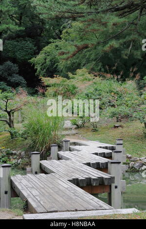 Passerelle en bois à motifs Zig Zag sur pilotis enjambant un canal entre deux étangs dans le sud de la région de Ritsurin koen-ches Banque D'Images