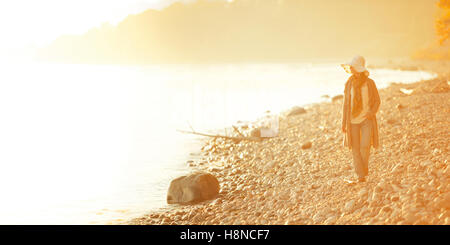 Woman walking along rocky shore au coucher du soleil Banque D'Images