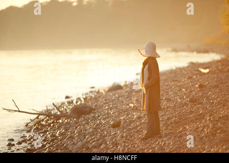 Woman walking along rocky shore au coucher du soleil Banque D'Images
