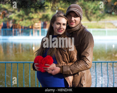 Happy pregnant couple hugging les uns les autres. Elle est titulaire d'une peluche en forme de cœur. Ils ont l'air heureux. Temps d'automne Banque D'Images