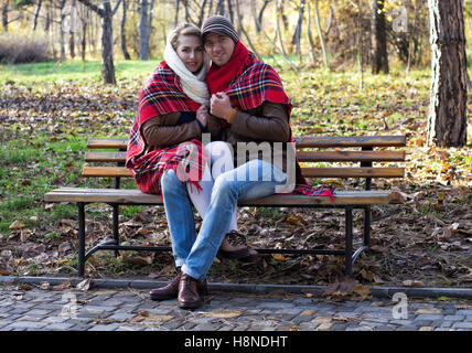 Jeune couple assis sur un banc dans le parc couvert de plaid/couverture. Saison d'automne. Banque D'Images