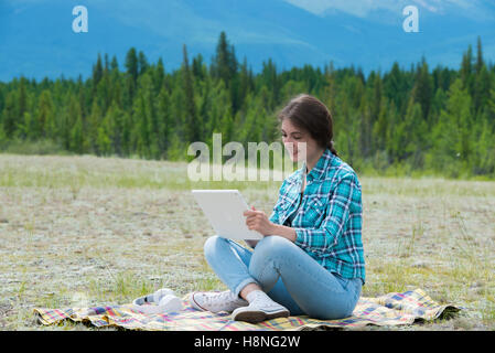 Belle jeune fille dans un champ sur les montagnes, à l'aide de tablet pc. Banque D'Images