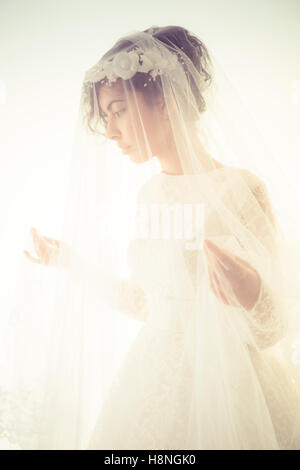 Suite Nuptiale photographie de mariage : Une jeune femme à la peau d'olive portant une robe de mariée blanche et un voile debout devant un fond blanc, UK Banque D'Images