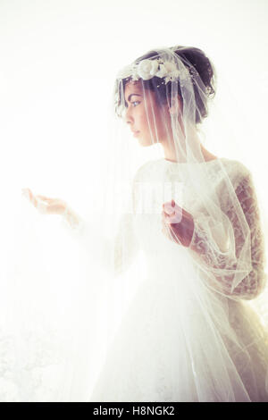 Suite Nuptiale photographie de mariage : Une jeune femme à la peau d'olive portant une robe de mariée blanche et un voile debout devant un fond blanc, UK Banque D'Images