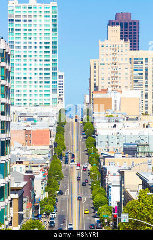 Téléobjectif lointain vue vers le bas de California Street Cable Car emblématique et l'extrémité de Bay Bridge entre les immeubles résidentiels sur Banque D'Images