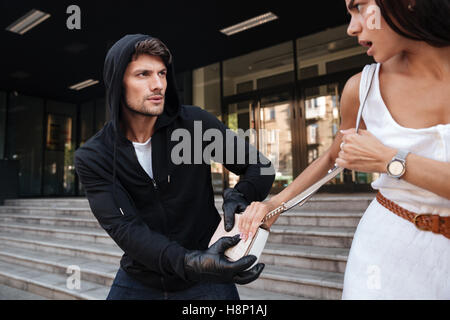 L'homme en noir voleur voler à capuche femme sac sur la rue Banque D'Images