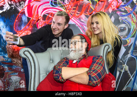 Utilisez uniquement rédactionnel Max Alan (à gauche) et prendre un Thorley Paige avec selfies modèle français Philippe Dumas comme il est dévoilé comme "hip" Nic, Canary Wharf est une version moderne des traditionnels le St Nicolas dans le cadre de leur pop-up Santa's Grotto pour adultes de Jubilé Place à Canary Wharf, Londres. Banque D'Images