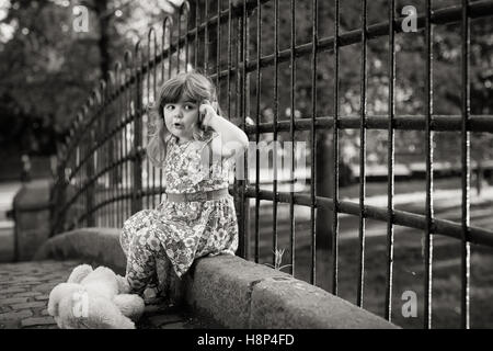 Cute little girl assis sur un pont faisant semblant de parler sur un téléphone mobile Banque D'Images