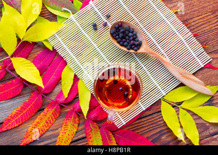 Infusion d'aubépine dans un bol en verre, une cuillère en bois avec des fruits secs et des panneaux de nattes de bambou sur la table avec un jaune vif et crimson Banque D'Images