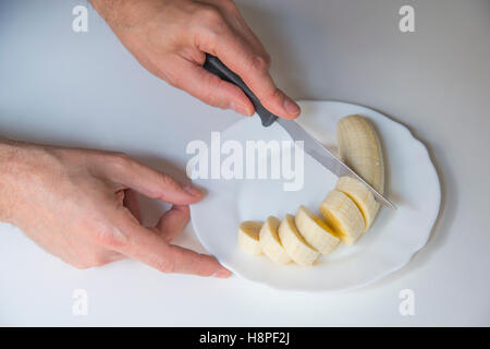 Man's hands couper une banane en rondelles. Banque D'Images