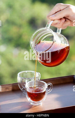 Verser un verre de thé dans une tasse sur un fond nature floue Banque D'Images