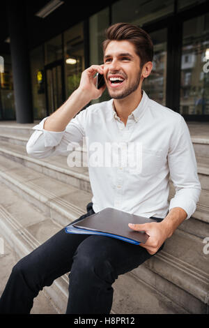 Happy young woman holding documents avec dossier et talking on cell phone Banque D'Images