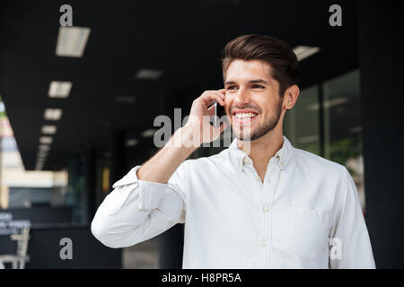 Portrait of happy handsome young businessman talking on mobile phone près de centre d'affaires Banque D'Images