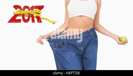 Image composite de mid section de slim femme portant des jeans trop grand holding an apple Banque D'Images