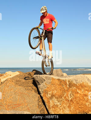 Mountain biker jumping à travers les rochers sur le mur du port de Staithes, Yorkshire du Nord Banque D'Images