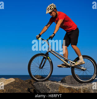 Mountain biker jumping à travers les rochers sur le mur du port de Staithes, Yorkshire du Nord Banque D'Images