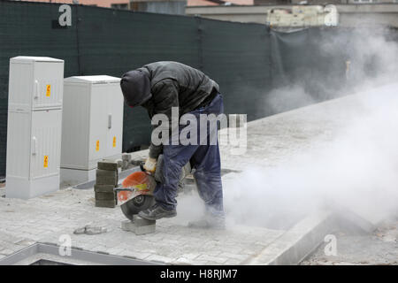 Travailleur utilise un tailleur de pierre pour couper les pavés en brique. Pavage en béton coupe à l'aide d'une rage de dents de scie de coupure. Pavé de scies Banque D'Images