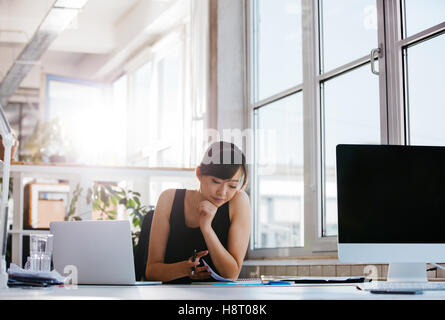 Tourné de belle jeune femme assise à son bureau en passant par certains documents. Asian businesswoman working in modern offic Banque D'Images