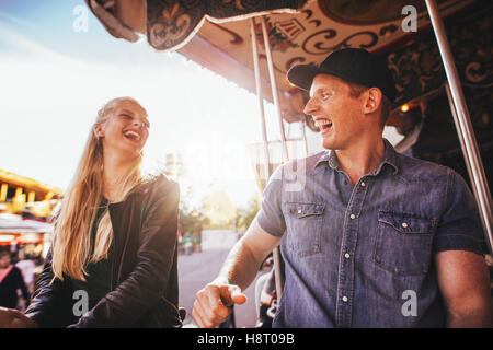 Laughing young friends riding sur carrousel dans le parc d'attractions. Smiling couple sur carousel ride. Banque D'Images