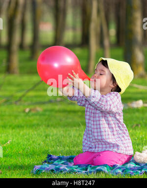 Petite fille du gonflage ballon rouge à l'extérieur Banque D'Images