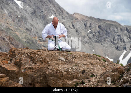 L'homme dans un kimono est assis en position du lotus sur le dessus de la montagne et de regarder les photos dans l'appareil photo. Banque D'Images