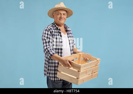 Personnes âgées agriculteur détenant une caisse vide en bois isolé sur fond bleu Banque D'Images