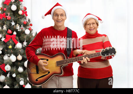 Heureux les aînés jouant de la guitare devant un arbre de Noël Banque D'Images