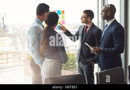 L'équipe entreprise multiraciale brainstorming permanent ensemble devant une grande fenêtre d'affichage lumineux à l'office en pointant sur un ensemble Banque D'Images