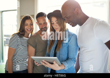 Groupe diversifié de quatre jeunes adultes attractif habillé de désinvolture en regardant quelque chose d'intéressant sur un ordinateur tablette Banque D'Images