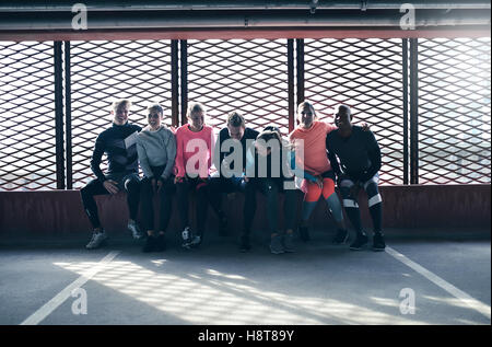 Groupe de jeunes sportifs assis ensemble et rire contre la fenêtre barrée sur un terrain de sport. Banque D'Images