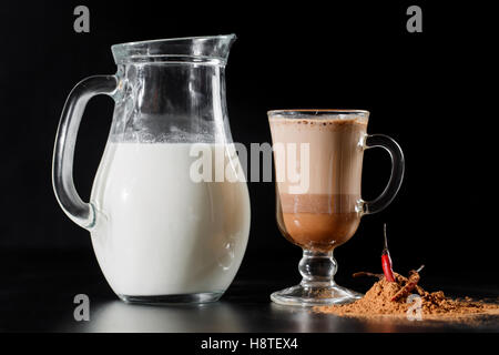 Le lait est de bouteille verseuse dans le verre sur fond noir. Banque D'Images