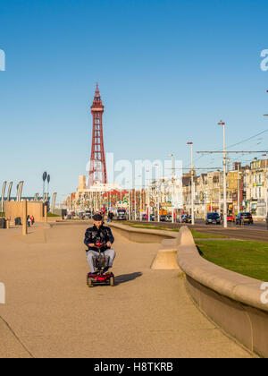 Old man riding scooter de mobilité électrique le long de la promenade de Blackpool avec en arrière-plan La tour de Blackpool, Lancashire, Royaume-Uni. Banque D'Images